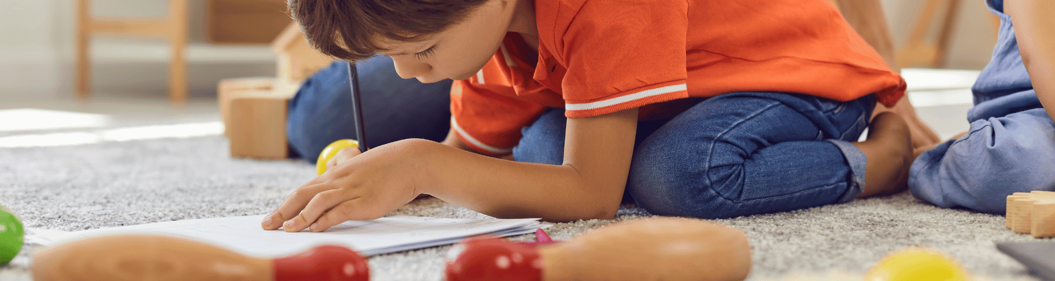 A young boy sits on the floor and draws.