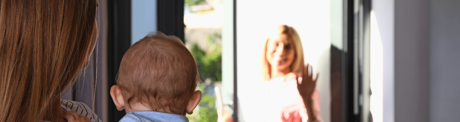 A nanny holding a baby watches a mother say goodbye.