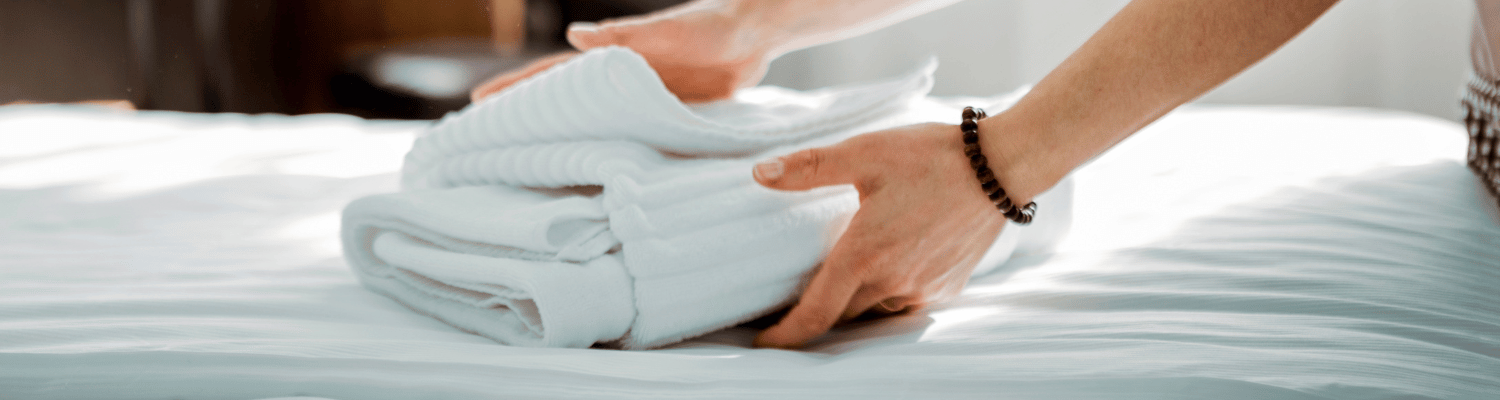 A woman puts folded linens on a bed.