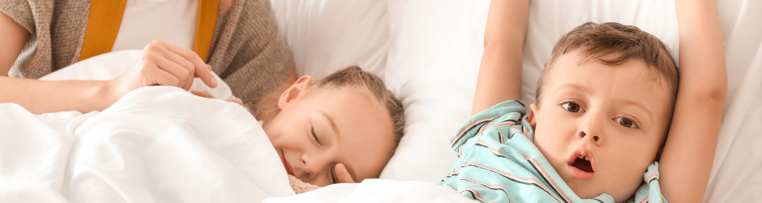 Two children are in a bed, one is asleep and the other is awake.